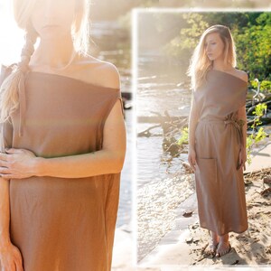 May include: Two women wearing a brown linen dress with a loose, flowing fit. The dress has a simple, off-the-shoulder neckline and a relaxed silhouette. The dress is shown in a natural setting, with one woman standing on a sandy beach and the other standing in a grassy field.