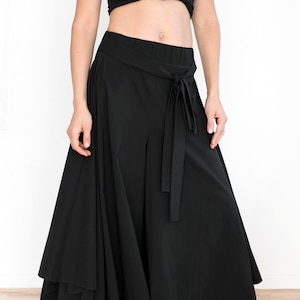 May include: Black wide-leg pants with a flowing, layered skirt design. The pants have a high waist and a tie belt.