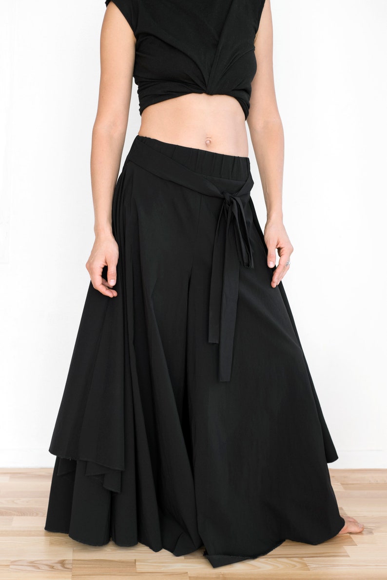 May include: Black wide-leg pants with a flowing, layered skirt design. The pants have a high waist and a tie belt.