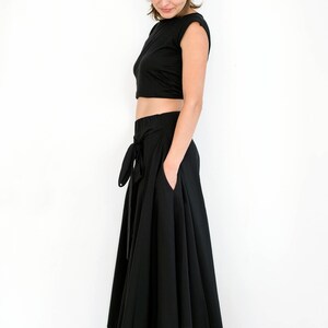 May include: A black crop top and a long black skirt with a wrap-style tie at the waist. The skirt has multiple layers and a flowing silhouette.