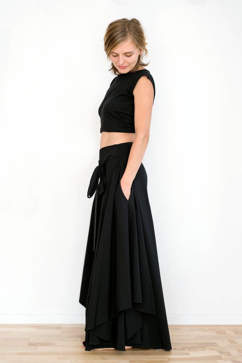May include: A black crop top and a long black skirt with a wrap-style tie at the waist. The skirt has multiple layers and a flowing silhouette.