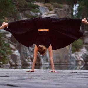 May include: A person in black clothing performs a handstand on a wooden surface. The person's legs are extended and their arms are straight. The background is a rocky, outdoor setting.