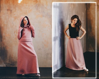 May include: Two women wearing long, dusty rose-colored skirts. The woman on the left is wearing a matching hooded sweatshirt. The woman on the right is wearing a black sleeveless top.