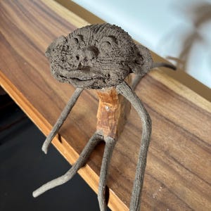 May include: A whimsical wooden sculpture of a monkey with a textured, brown clay head and long, twig-like limbs.
