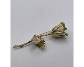 Könnte beinhalten: Eine goldfarbene Rosenbrosche mit einem einzelnen Blatt. Die Rose ist stilisiert und hat eine strukturierte Oberfläche.