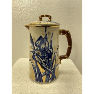 Könnte beinhalten: Eine weiße Keramikkanne mit einem blauen und goldenen Blumendesign. Die Kanne hat einen braunen Bambusgriff und einen goldenen Deckel.