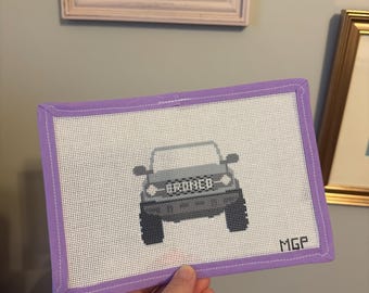 Può includere: Un ricamo a mano con un design di SUV Bronco grigio. Il veicolo è centrato su una tela bianca, incorniciata da un bordo lavanda. La parola "BRONCO" è ricamata sopra l'auto. Le iniziali "MGP" sono in basso a destra.