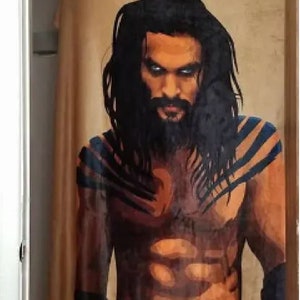 May include: A shower curtain featuring a close-up portrait of a man with long black hair and a beard. He has a muscular physique and is wearing a black loincloth. The background is a brown and gold color.