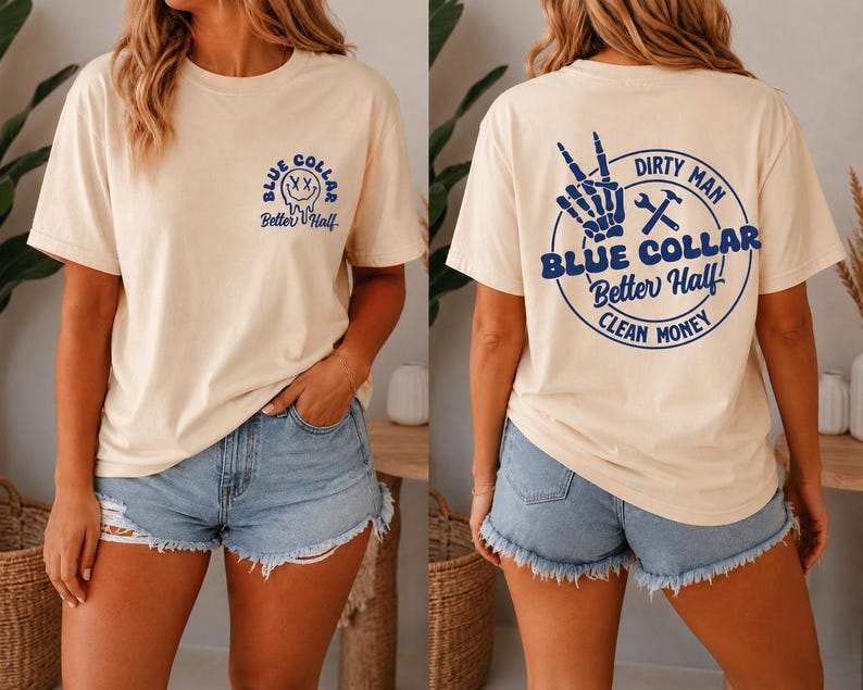 Puede incluir: Una camiseta de manga corta color crema con un peque&ntilde;o gr&aacute;fico azul en el pecho que muestra una cara sonriente derriti&eacute;ndose y el texto Blue Collar Better Half. La parte trasera muestra un gran gr&aacute;fico circular azul con una mano esquel&eacute;tica, herramientas y texto.