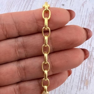 May include: A gold chain bracelet featuring a series of interconnected oval links. Each individual link has a distinct hammered, textured surface finish that catches the light, creating a repeating pattern along the length of the jewelry piece.