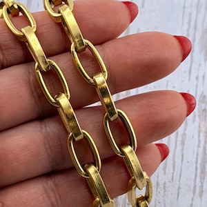 May include: Close-up of two gold-colored chain necklaces. The chains have large, oval links connected by rectangular bars. The jewelry is displayed against a light-colored background. The chains are a warm, bright gold color.