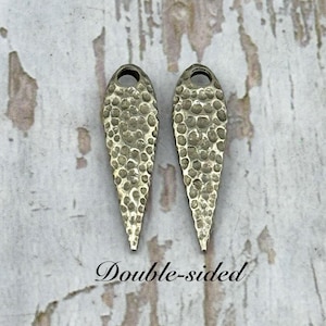 Pu&ograve; includere: Due orecchini bifacciali color argento con una texture martellata. Ogni orecchino ha la forma di una goccia con un piccolo foro nella parte superiore. Il testo "Double-sided" &egrave; scritto in corsivo sotto.