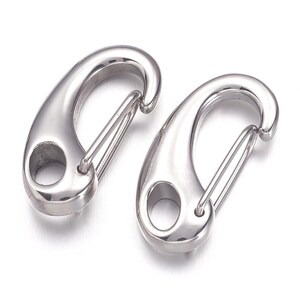 May include: Two polished, silver-colored spring snap hooks. Each hook has a rounded body with a hole and a spring-loaded gate. The hooks are designed for quick and secure attachment of items.