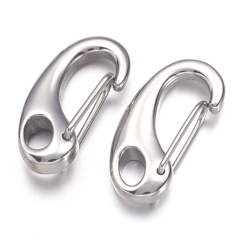 May include: Two polished, silver-colored spring snap hooks. Each hook has a rounded body with a hole and a spring-loaded gate. The hooks are designed for quick and secure attachment of items.