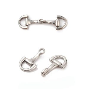 May include: Silver-toned metal horse bit charms. The charms are in two different styles, one with a connecting chain and the other with a loop. The charms have a polished finish and are set against a white background.
