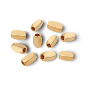 May include: A collection of gold-colored, barrel-shaped beads with a polished finish. Each bead has a cylindrical hole running through its center, suitable for stringing. The beads are scattered against a white background.