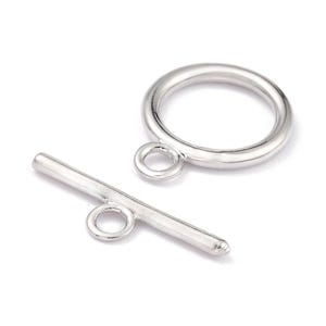 May include: A silver-toned toggle clasp set consisting of a circular ring with a small attached loop and a straight bar component with a centered loop. Both pieces feature a smooth, polished metallic finish and are designed for jewelry assembly.
