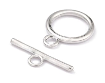Könnte beinhalten: Ein silberfarbenes Knebelverschluss-Set, bestehend aus einem kreisförmigen Ring mit einer kleinen angebrachten Öse und einem geraden Stabelement mit einer mittigen Öse. Beide Teile haben eine glatte, polierte Metalloberfläche.