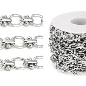 May include: Shiny silver-colored chain in a roll and three close-up sections. The chain links are oval-shaped with a small ball on each side, connected by a bar. The roll of chain is on a white spool.