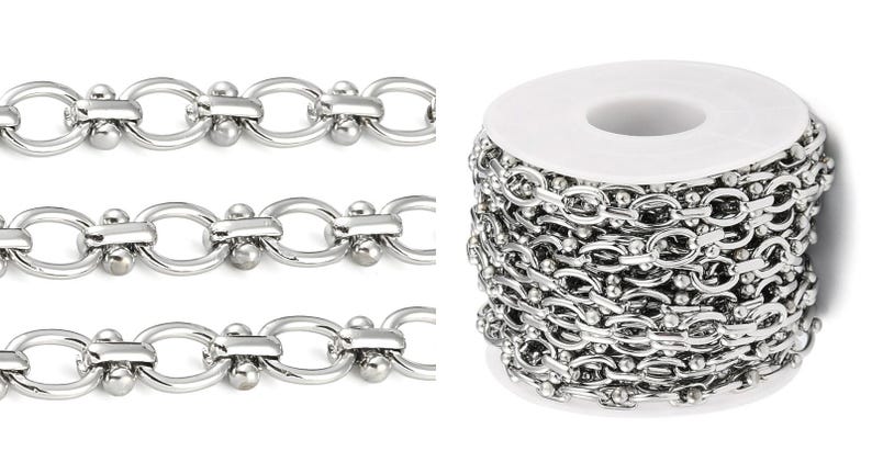 May include: Shiny silver-colored chain in a roll and three close-up sections. The chain links are oval-shaped with a small ball on each side, connected by a bar. The roll of chain is on a white spool.