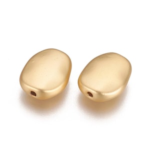 May include: Two gold-colored oval-shaped beads with a hole in the center. The beads have a matte finish.