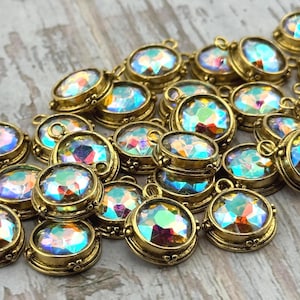 May include: A collection of iridescent oval-shaped crystal charms with gold-colored metal settings. The charms have a loop at the top for attaching to jewelry. The crystals reflect multiple colors, and the metal has a decorative edge.