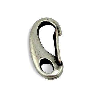 May include: A silver-colored oval carabiner clip with a spring-loaded gate. The clip has a circular opening at the bottom and a slightly textured surface. The metal has a worn, vintage appearance.