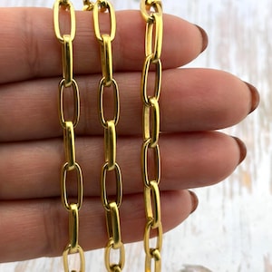 May include: Close-up of three gold-colored chain necklaces with elongated oval links. The chains are held against a neutral background. The chains are a bright, shiny gold color.