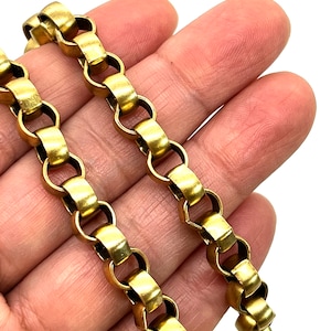 May include: Close-up of a gold-colored chain necklace with a repeating rectangular link design. The chain is held in a hand against a white background, highlighting the warm tones of the metal.