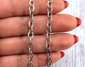 May include: Two silver-colored chain necklaces with oval links are displayed. The chains are held against a light-colored background. The chains are made of metal and have a slightly tarnished appearance.