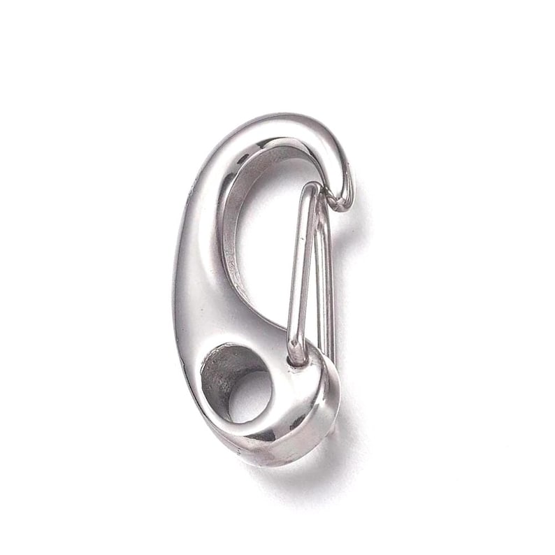 May include: A shiny, silver-colored carabiner clip. The clip has a rounded, oval shape with a spring-loaded gate. It features a small hole at the base and is designed for secure attachment. The carabiner is made of metal.