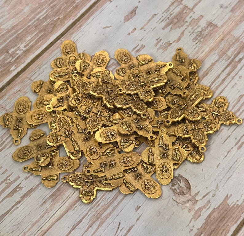Peut inclure: Un ensemble de petites croix en m&eacute;tal dor&eacute;. Chaque croix pr&eacute;sente des images religieuses d&eacute;taill&eacute;es et une petite boucle en haut pour l'enfilage. Les croix sont &eacute;parpill&eacute;es sur une surface claire &agrave; grain de bois.