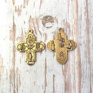 Peut inclure: Deux pendentifs en forme de croix religieuses dor&eacute;es. Chaque croix pr&eacute;sente des figures et des symboles religieux d&eacute;taill&eacute;s. Les croix sont pr&eacute;sent&eacute;es sur une surface en bois clair vieilli.