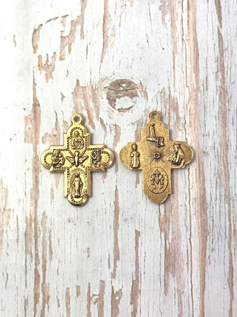 Peut inclure: Deux pendentifs en forme de croix religieuses dor&eacute;es. Chaque croix pr&eacute;sente des figures et des symboles religieux d&eacute;taill&eacute;s. Les croix sont pr&eacute;sent&eacute;es sur une surface en bois clair vieilli.