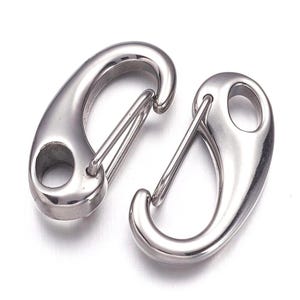 May include: Two polished, silver-colored spring snap hooks. Each hook has a curved body with a spring-loaded gate and an eyelet for attachment. The hooks are designed for secure fastening and are suitable for various applications.