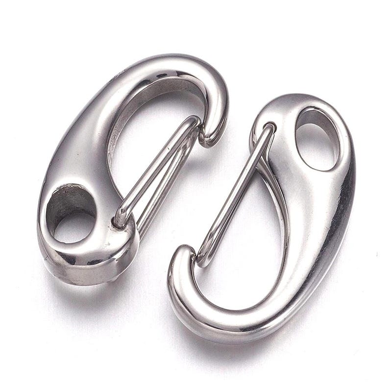 May include: Two polished, silver-colored spring snap hooks. Each hook has a curved body with a spring-loaded gate and an eyelet for attachment. The hooks are designed for secure fastening and are suitable for various applications.