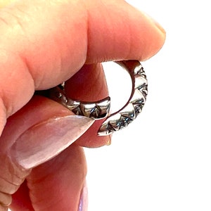 May include: A silver ring with a textured, geometric design. The ring is open and has a pointed edge.