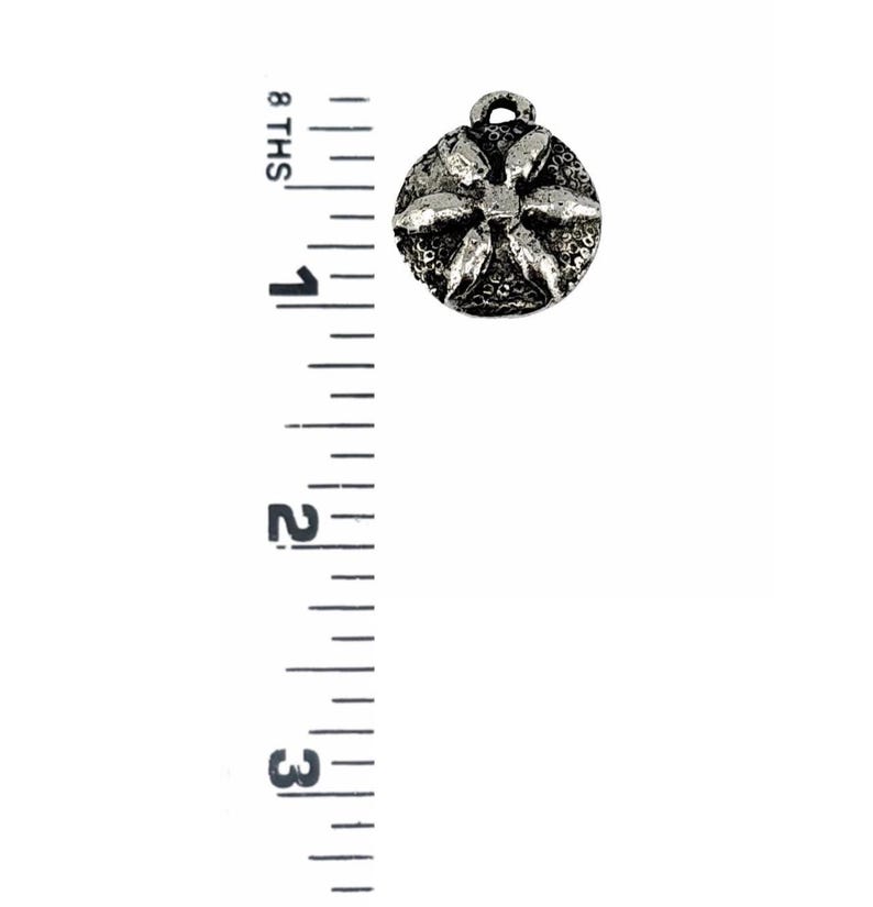 Op de afbeelding: Een kleine, ronde, zilverkleurige metalen bedel met een bloemmotief. De bedel heeft een lus aan de bovenkant om aan een ketting of andere sieraden te bevestigen. De bedel heeft een diameter van ongeveer 2,5 cm.