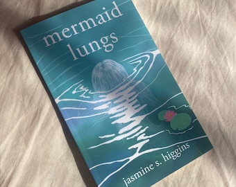 May include: A teal blue book with the title "mermaid lungs" in white text. The cover features a white line drawing of a mermaid swimming underwater with a pink water lily. The author's name, "jasmine s. higgins", is printed in white at the bottom of the cover.