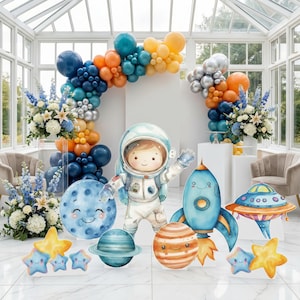 Könnte beinhalten: Ein Party-Deko-Set zum Thema Weltraum mit einem großen Ballonbogen in Blau, Orange und Silber. Enthält Pappaufsteller eines lächelnden Astronauten, einer blauen Rakete, eines UFOs, eines Mondes, eines Planeten und mehrerer Sterne.