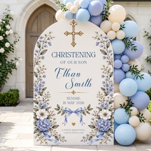 May include: An arched christening sign for Ethan Smith featuring a gold cross, blue floral illustrations, and a blue ribbon. The text reads: CHRISTENING OF OUR SON, Ethan Smith, SUNDAY, 18 MAY 2026, A SWEET BEGINNING, A BEAUTIFUL LIFE. Decorated with blue and cream balloons.