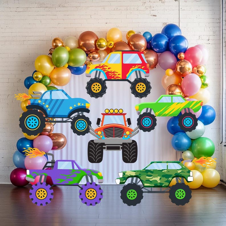 Op de afbeelding: Een verzameling kleurrijke monstertruck-uitsparingen met vlam- en sterontwerpen. De trucks zijn in verschillende kleuren, waaronder rood, blauw, groen, paars en oranje. Een ballonnenboog in goud, blauw, roze en groen omringt de trucks.