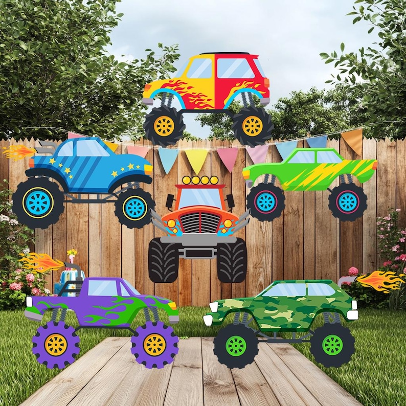 Op de afbeelding: Een verzameling van zes kleurrijke monster truck uitsparingen. De trucks zijn in verschillende kleuren, waaronder rood, geel, blauw, groen, oranje en paars, met vlam- en sterontwerpen. Ze hebben grote zwarte banden met kleurrijke velgen, tegen een houten hek en groen gras.