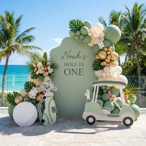 Peut inclure: Un panneau de fond vert sauge avec le texte Noah's HOLE IN ONE, orné d'une arche de ballons vert sauge, crème et dorés. Inclut des découpes d'un sac de golf, d'une voiturette de golf et d'une balle de golf blanche sur fond océanique.
