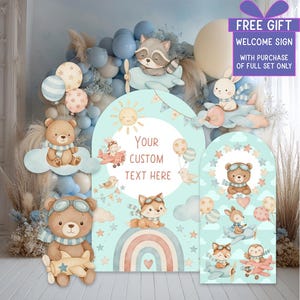May include: A baby shower backdrop set with cartoon animals in aeroplanes, balloons, and a rainbow. The backdrop includes the text "Your Custom Text Here" and "FREE GIFT WELCOME SIGN WITH PURCHASE OF FULL SET ONLY". The colour palette includes pastel blues, pinks, and browns.