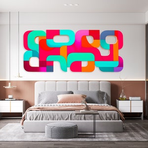 May include: A modern bedroom with a white bed, a gray rug, and a colorful abstract wall art piece. The art piece is made of geometric shapes in shades of pink, orange, blue, and green.