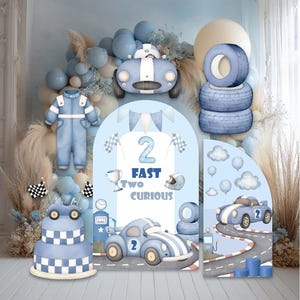 May include: A light blue race car themed birthday party backdrop with a cake, race cars, tires, and balloons. The text on the backdrop reads "2 Fast Two Curious". The backdrop has a checkered flag and a racing suit.