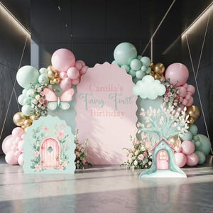 May include: A party backdrop set featuring a large pink scalloped sign with the text Camila's Fairy First Birthday, surrounded by pastel pink, mint green, and gold balloons, floral accents, a butterfly cutout, and two fairy house panels.