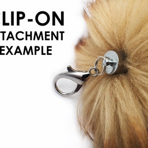 May include: A close-up of a clip-on attachment for a fluffy, brown pom-pom. The clip is silver and has a loop for attaching to a bag or other item. The text "CLIP-ON ATTACHMENT EXAMPLE" is visible in the image.