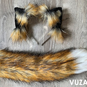 May include: A set of fox tail and ears costume accessories. The tail is brown, black, and white with a fluffy texture. The ears are attached to a headband and are brown, black, and white with a fluffy texture.